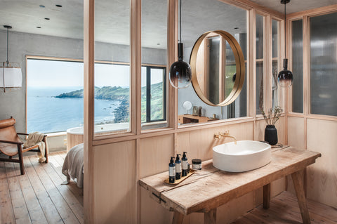 Photograph of Ukiyo interior with a focus on the larch cladding which surrounds a minimalist bathroom, looking out over the double debroom and floor to ceiling window.  An emerald seascape backdrop to the scandinavian inspired interior.