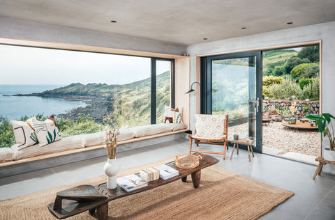 Photograph of Ukiyo interior, minimal scandi aesthetic with incredible wall size window looking out onto emeral sea and coast of the Lizard in Cornwall.