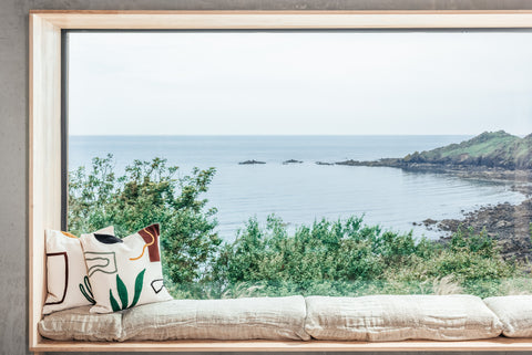 Full width photograph of floor to ceiling window, framing the coast and emerald sea of the Lizard peninsula.