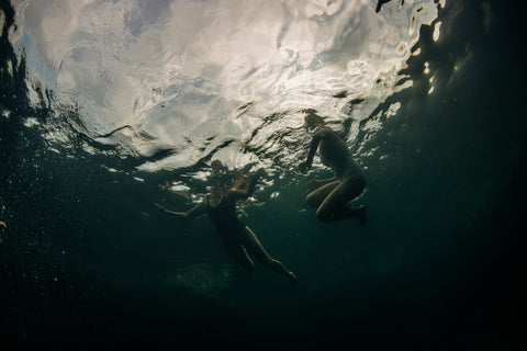 Underwater photograph of two swimmers, lit from above.