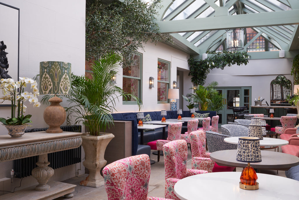 Bright upholstered chairs and tropical foliage deck out the sun-filled Orangery at Stanwell House Hotel.