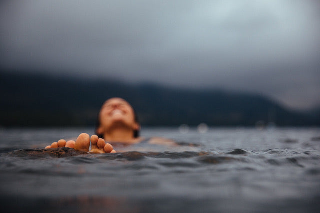 Photograph of swimmer floating on the top of lake, smiling, toes out of the water.