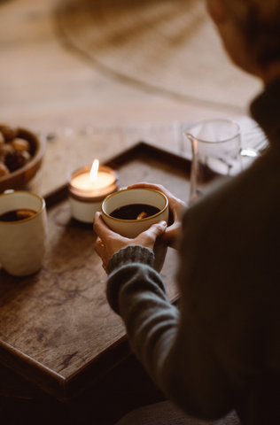 Candle and low light, hands holding mug of steaming mulled wine.