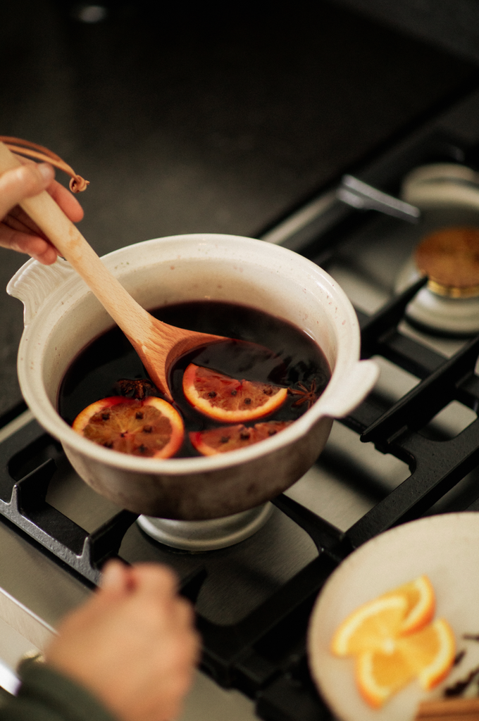Pot of mulled wine gently warming up on a gas hob, oranges and spices being mixed through.
