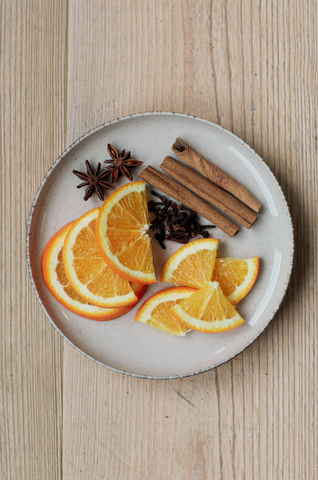 Slices of orange, star anise, cloves and cinnamon sticks arranged on plate.