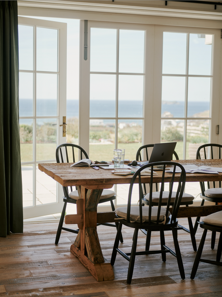 Long wooden dining table with chairs with glass doors opening out to a lawn and seaview at Atlanta Trevone