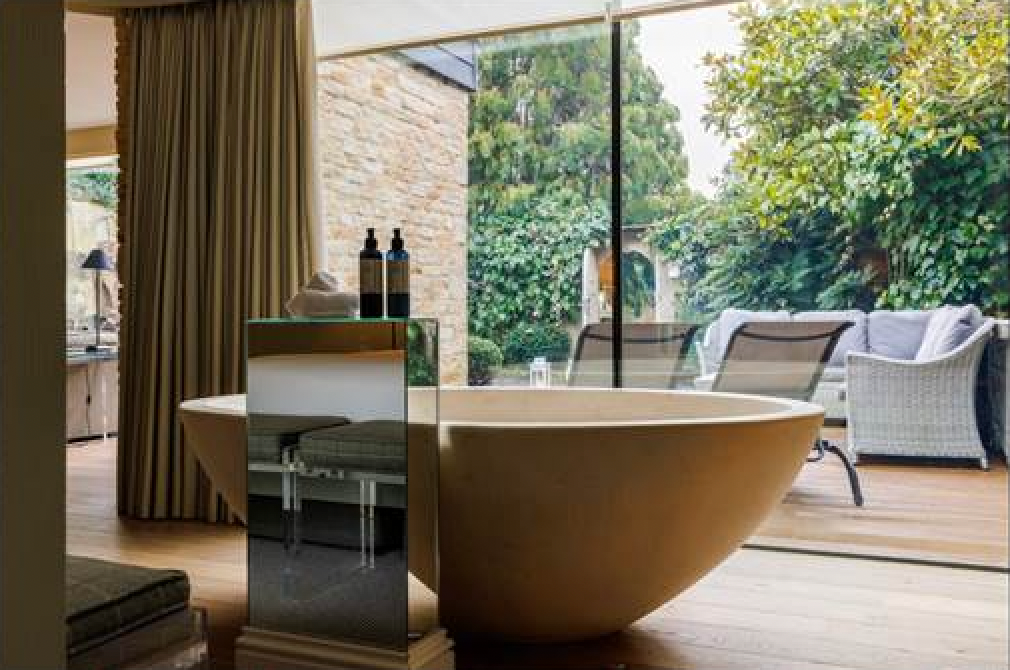 Bathroom with standalone bath, looking out onto garden through large glass window.