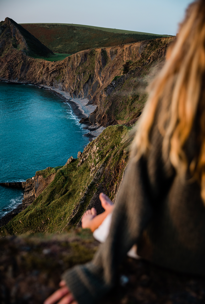 Walker sat down with back to camera looking out to sea, aqua marine water and waves down below.