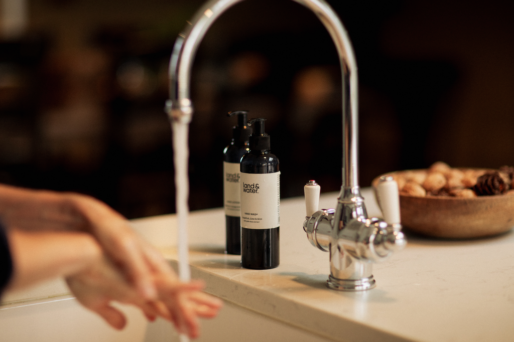 land&water Hand Duo products pictured on kitchen top next to sink with model washing hands.
