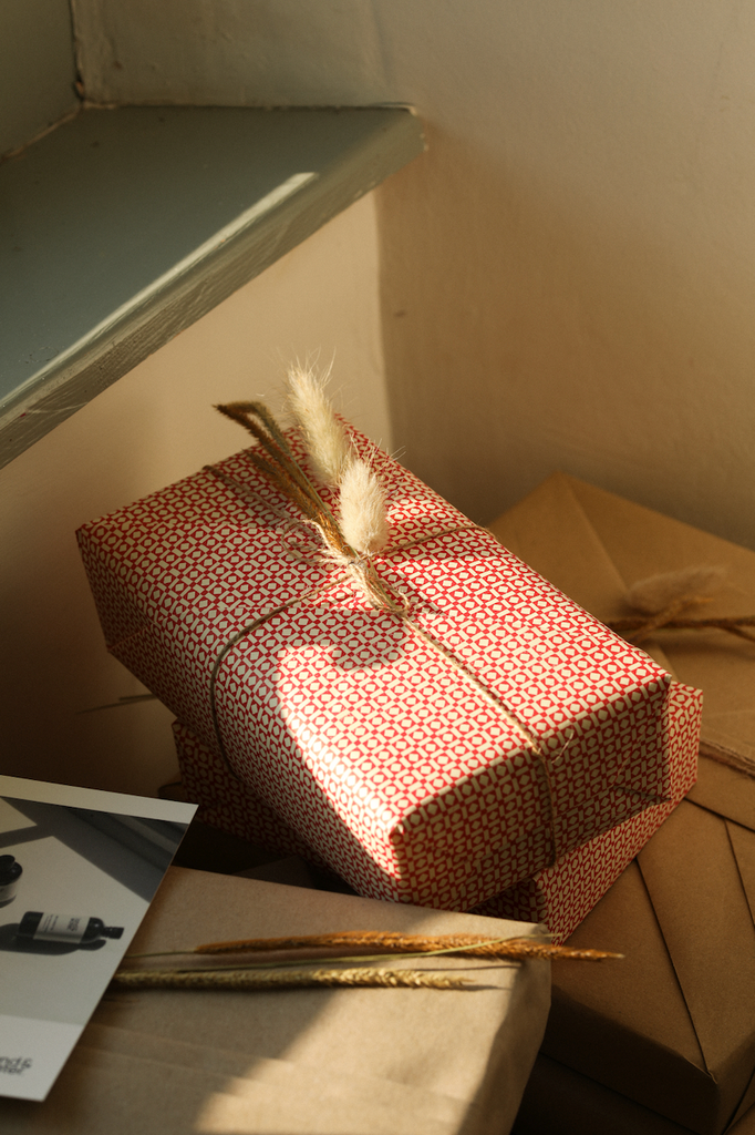Presents wrapped in brown paper with natural decorations such as dried grasses tucked inbetween string. Presents sat in windowsil in natural light.