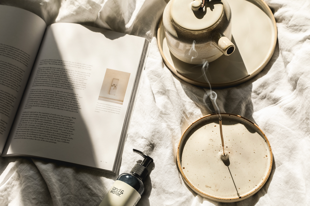 Calm bed linen scene with magazine open, hot pot of tea and incense burning.