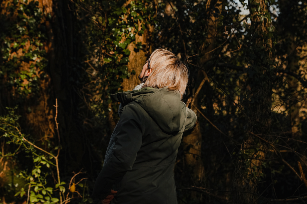 Land and Water founder, Pix Ashworth, standing in dappled woodland light.