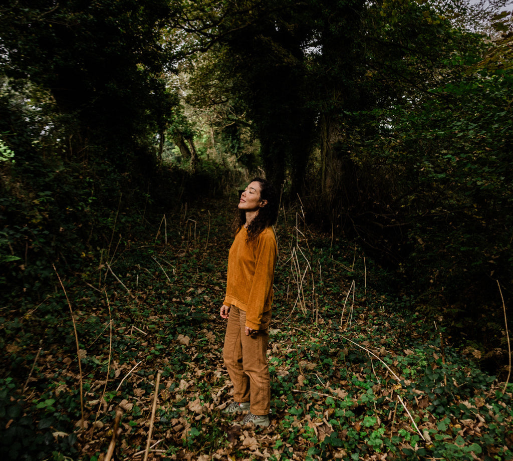 Woman stands in woodland clearing and soaks up dappled winter sun.