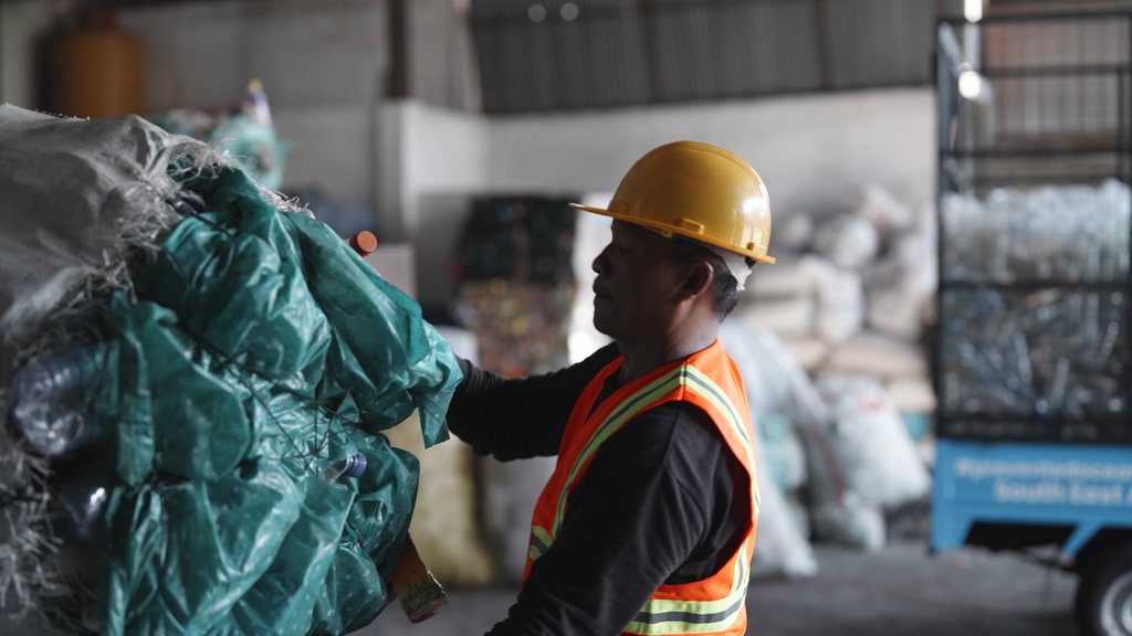 Image shows a man in high-vis collecting and recycling waste plastic ready to make into Land and Water packaging.