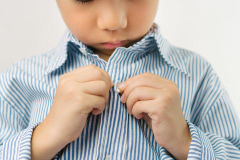 Image of young boy buttoning his dress shirt