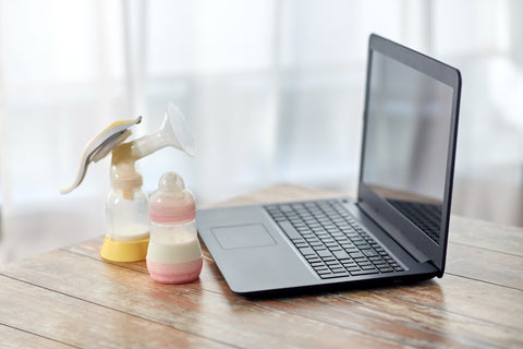 breast pump and baby bottle on desk next to laptop to indicate concept of pumping at work