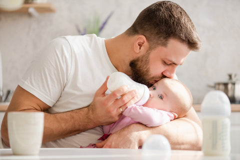 dad feeding a bottle to his baby and kissing the baby's head