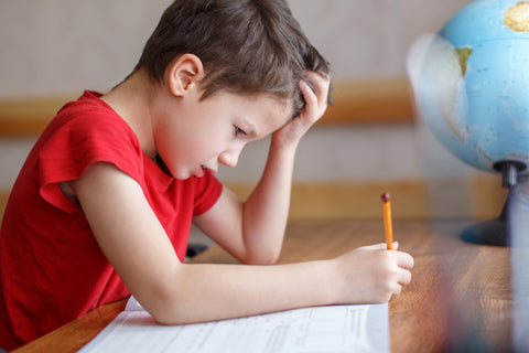 Image of elementary-age school boy at desk, frustrated by homework