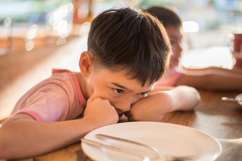 boy at table with empty dish to signify food insecurity for families