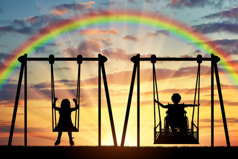 silhouette of two children on a swing set, one in a wheelchair, with rainbow overhead