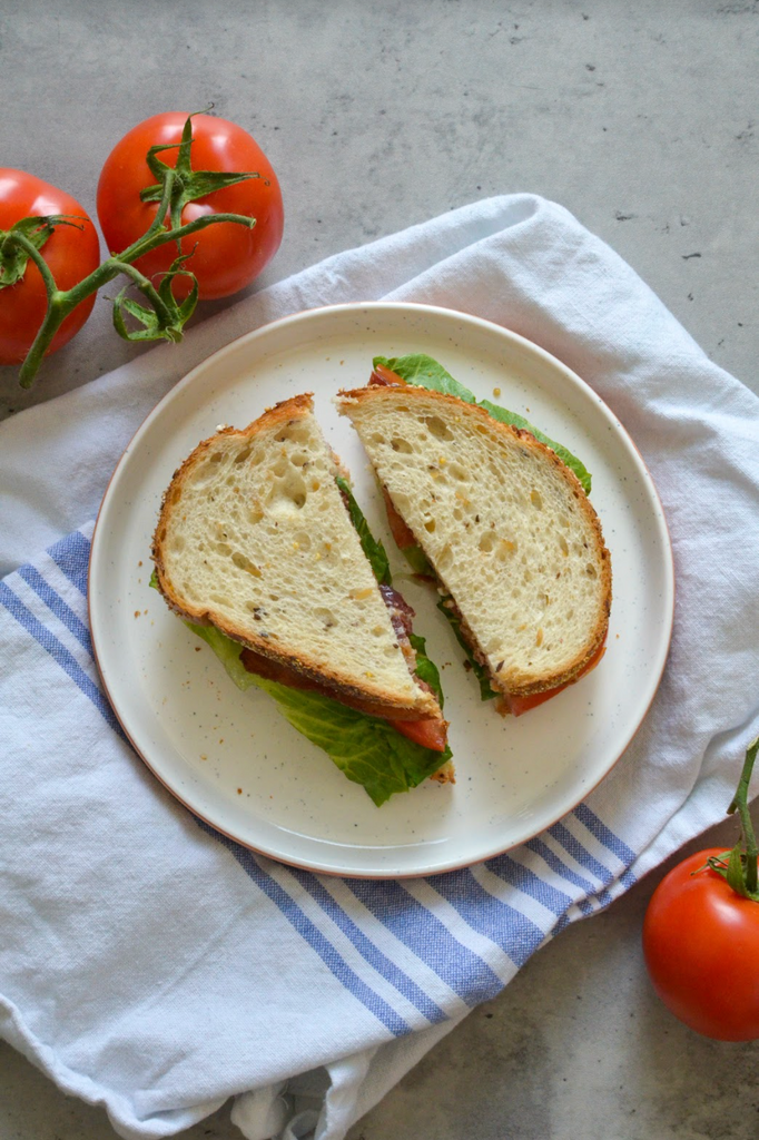 classic BLT, cut diagonally, on plate and next to tomatoes 