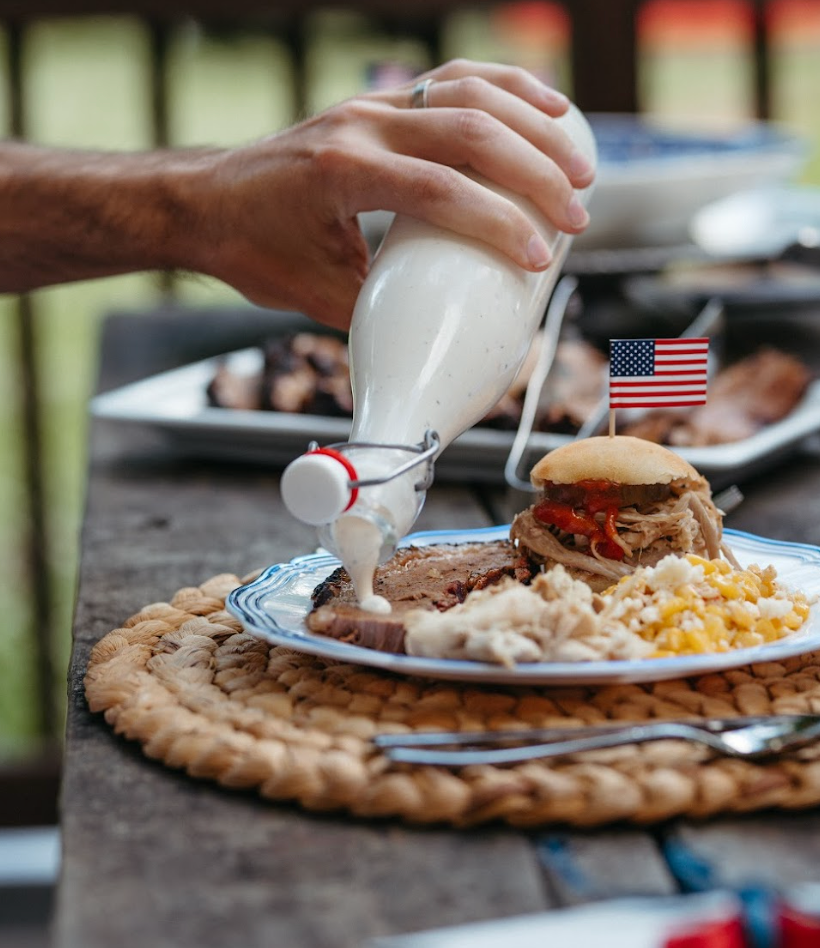 person pouring white sauce onto plate at a barbeque