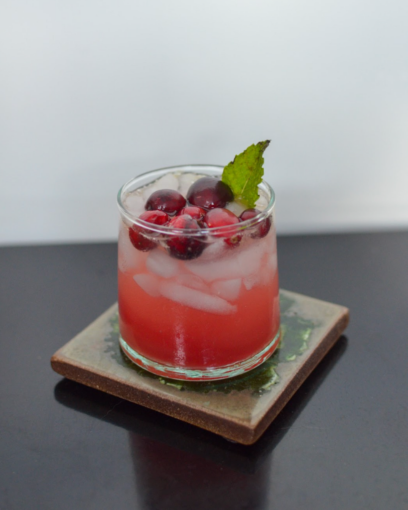 glass of cranberry mocktail with whole cranberries and mint leaf on top