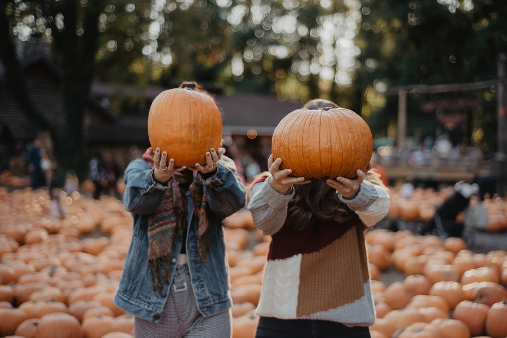 two people holding pumpkins in front of their faces