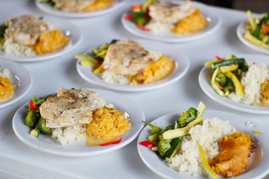 Table filled with plates of chicken, rice, and vegetables