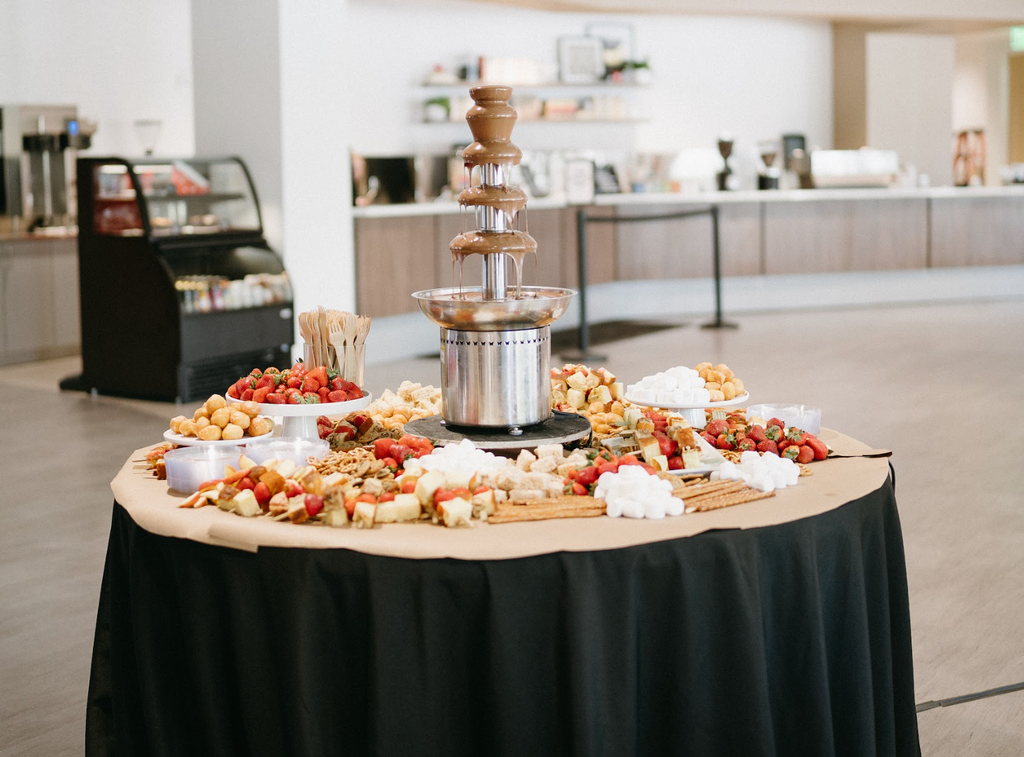 Table with chocolate fountain surrounded by dessert items and fresh fruits