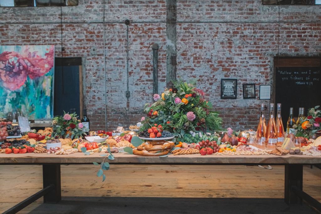 large table filled with various foods, flowers, and wine