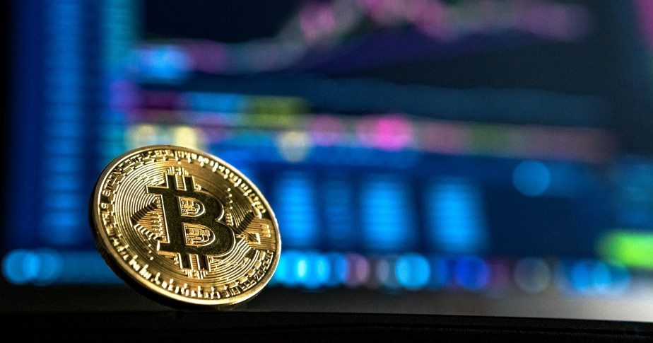 Een goudkleurige Bitcoin met op de achtergrond de beursvloer