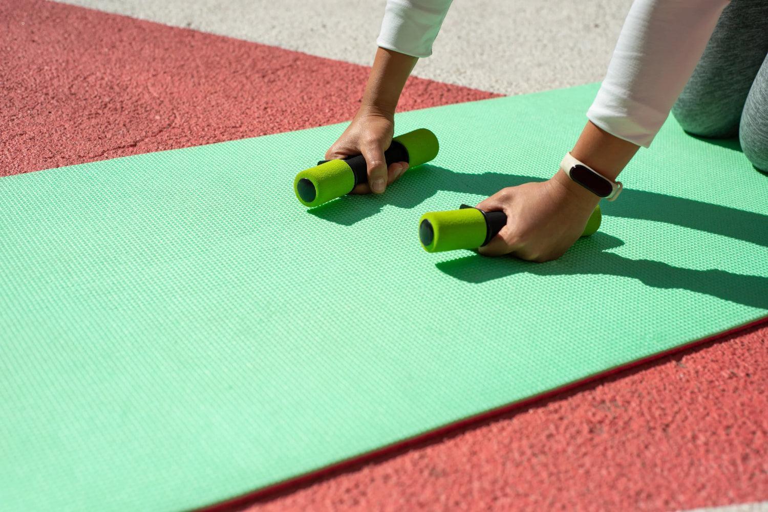 Een persoon buigt over een yogamat met kleine handgewichten