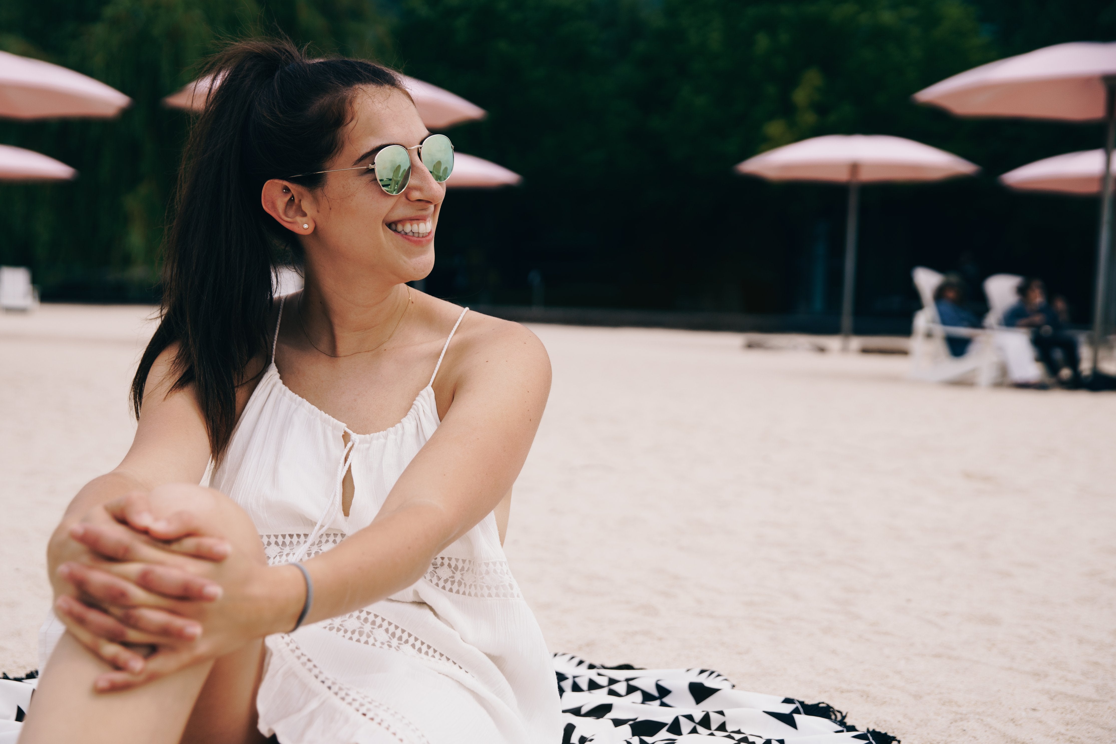 Lachende vrouw met zonnebril zit op het strand