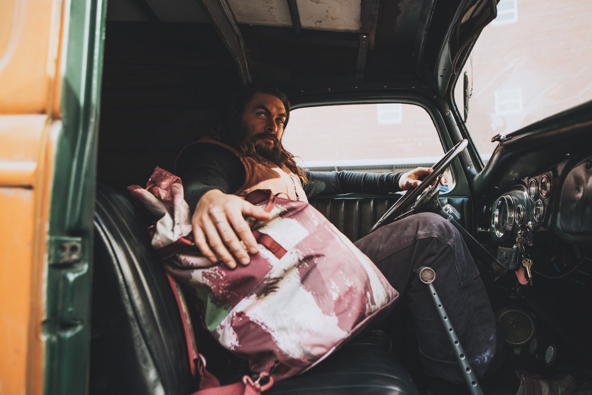 Jason Momoa is shown in an old car holding the So iLL x On The Roam eco camo 45L dirt bag is shown at elephant rocks state park