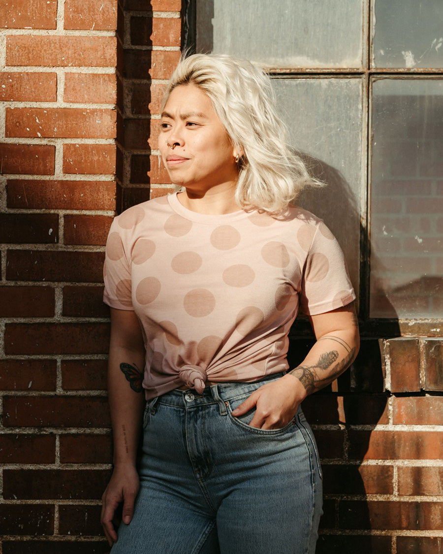 a woman wears the so ill x on the roam dirty pink polka dot tee against a brick wall