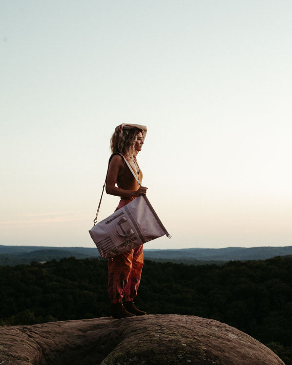 a woman overlooks a scenic range while wearing jason momoa's dirty pink dirt bag - a so ill and on the roam collaboration