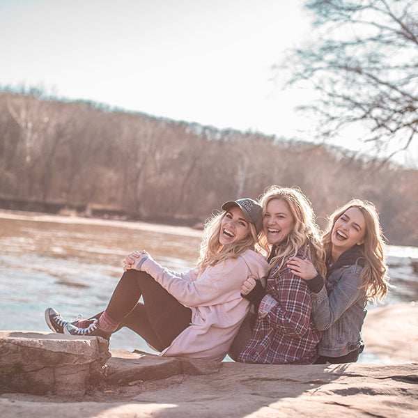 3 girls sitting outdoors by a river