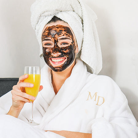 Girl at a spa with a face mask and white robe on.