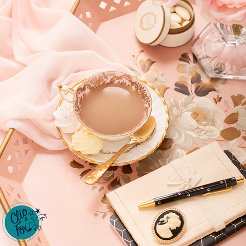 Pink vintage tea tray with blush pink chiffon scarf, vintage tea cup and saucer, black pen and notebook, with cream writing paper