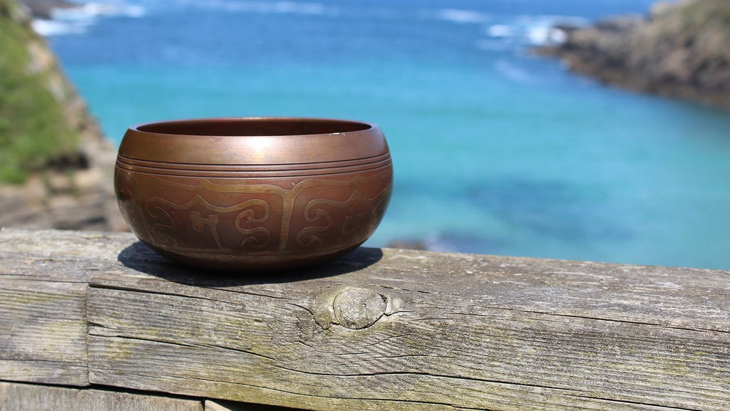 Un bol tibétain gravé de mantras sacrés, déposé devant un lac.