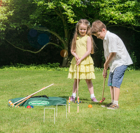 Two children playing croquet on a grass lawn