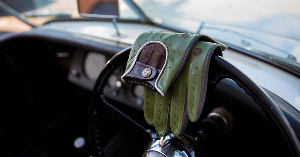 A pair of men's green and grey leather driving gloves draped over a steering wheel