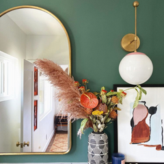 Olive green bathroom with an oversized brass wall sconce with pink accents