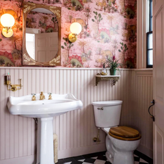 Retro Bathroom makeover features brass and glass wall sconce, pink wallpaper, black and white flooring