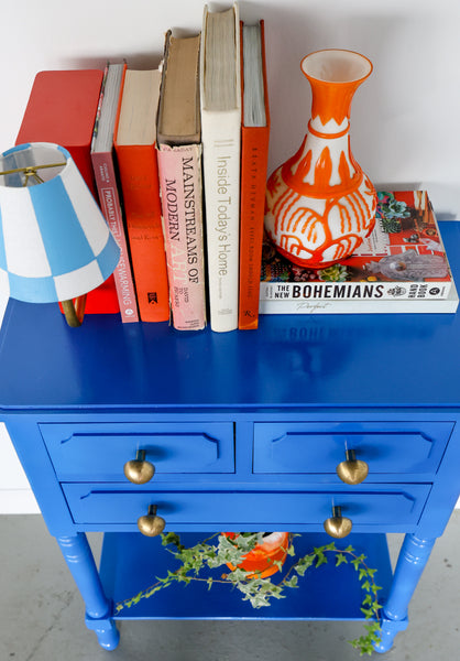 Brass mushroom knobs on blue end table with orange lampshade milton and books