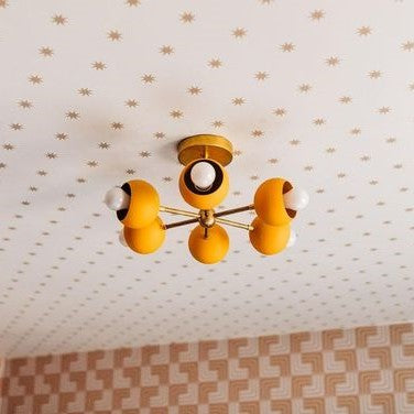 Mustard & Bras Loa Carousel Flushmount ceiling light for a low 8 foot ceiling room that has star-patterned wallpaper.  Lighting is by Sazerac Stitches in the colorway of mustard and brass