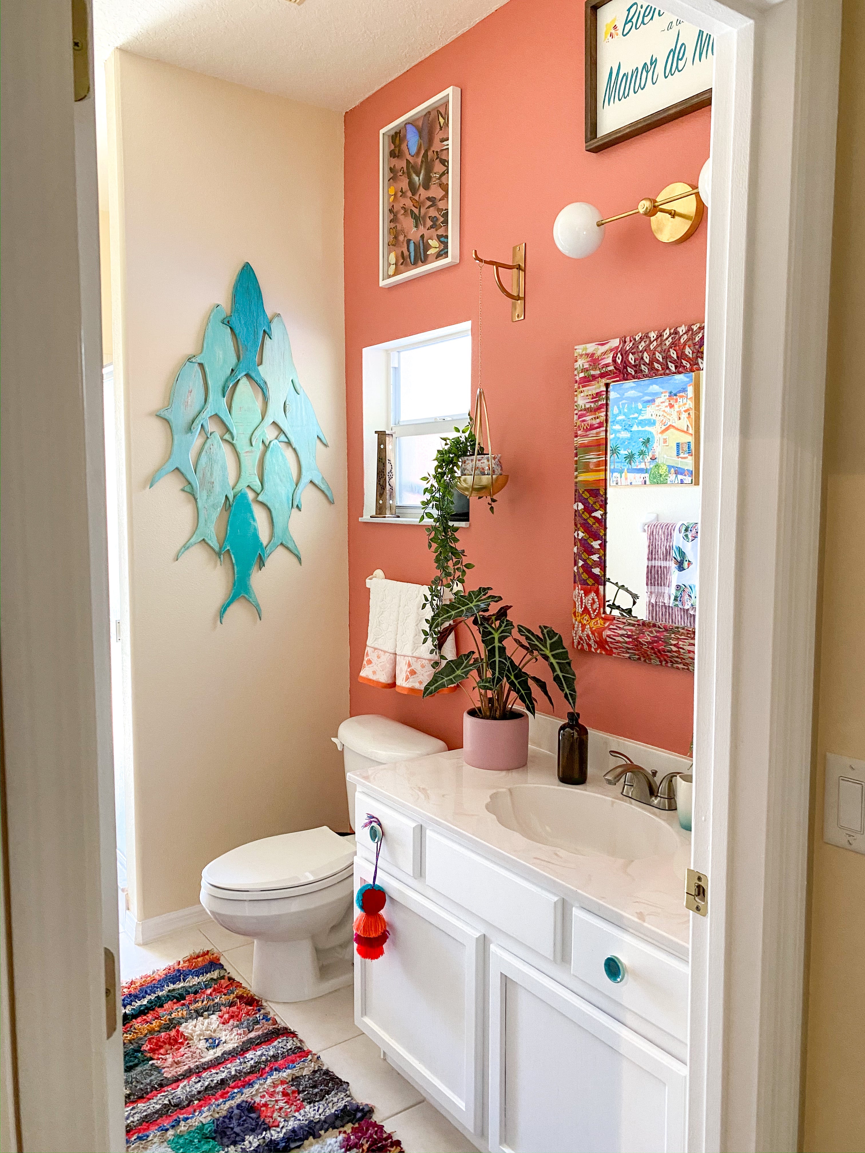 Peach and turquoise tropical bathroom design with gallery wall of pictures and plants