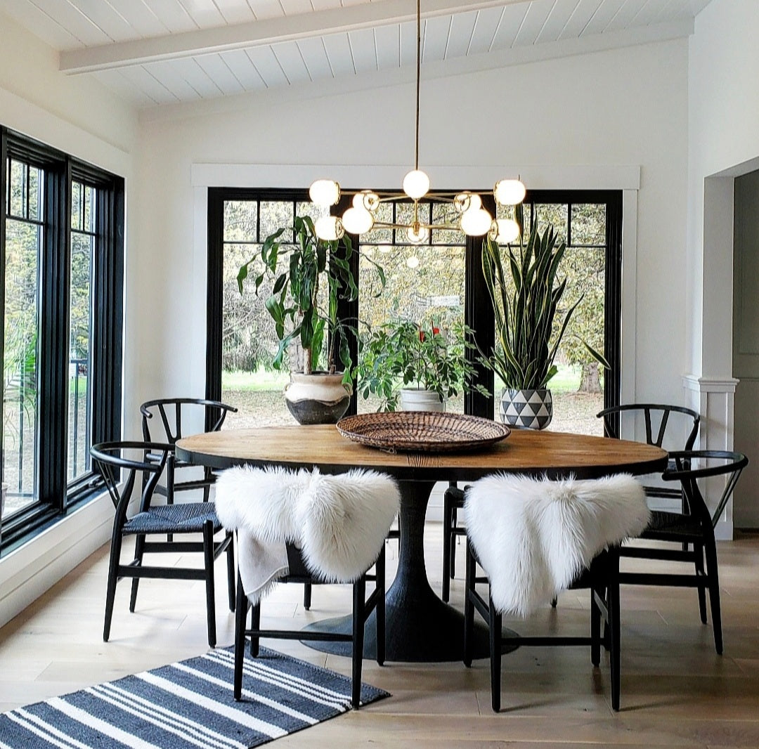 Farmhouse style dining room with a brass and glass chandelier over a wood pedestal table and black chairs.