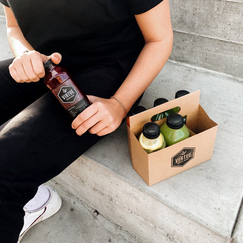 A Virtue juice cleanse on a concrete staircase, with a person holding a beet juice bottle.